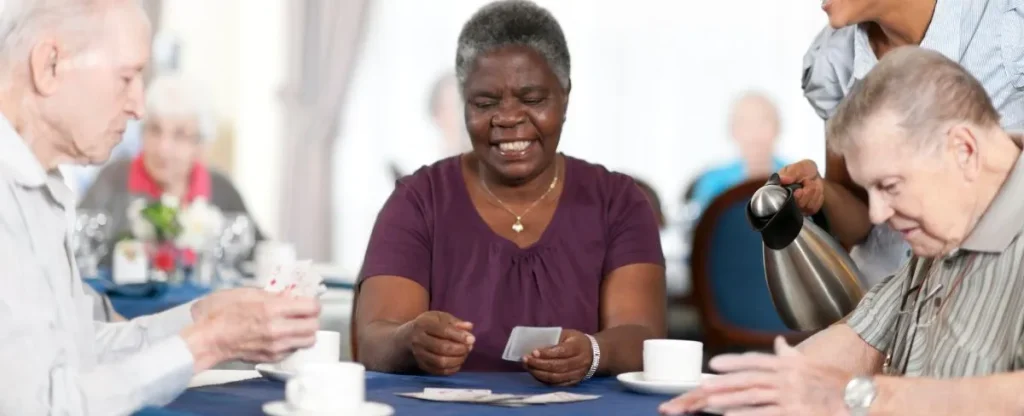 A group of seniors play cards around a table at an assisted living community.
