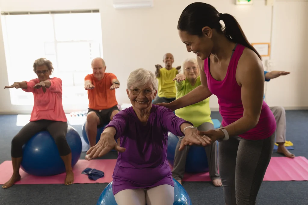A women in an assisted living community helping seniors with aerobics in a gym. community.